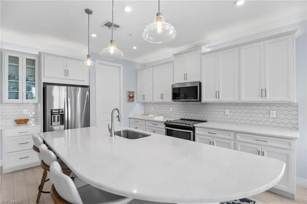 a kitchen with stainless steel appliances a stove a sink a microwave a refrigerator and white cabinets with wooden floor