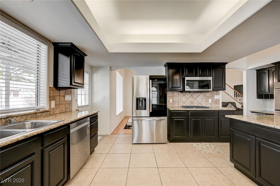 2955 El Camino Road Las Vegas, NV 89146 - Photo 26 of 99 Kitchen featuring backsplash, stainless steel appliances, light stone counters, light tile patterned flooring, and dark cabinetry