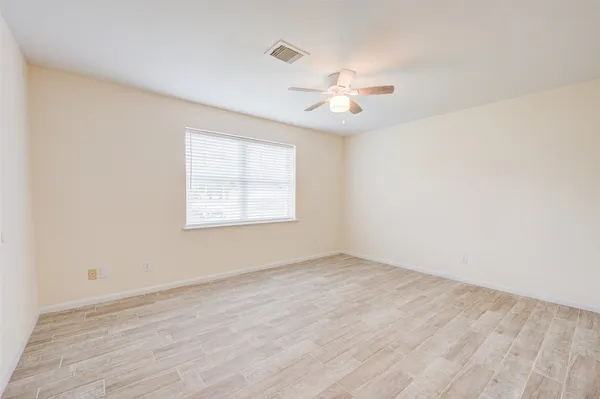 an empty room with wooden floor fan and windows