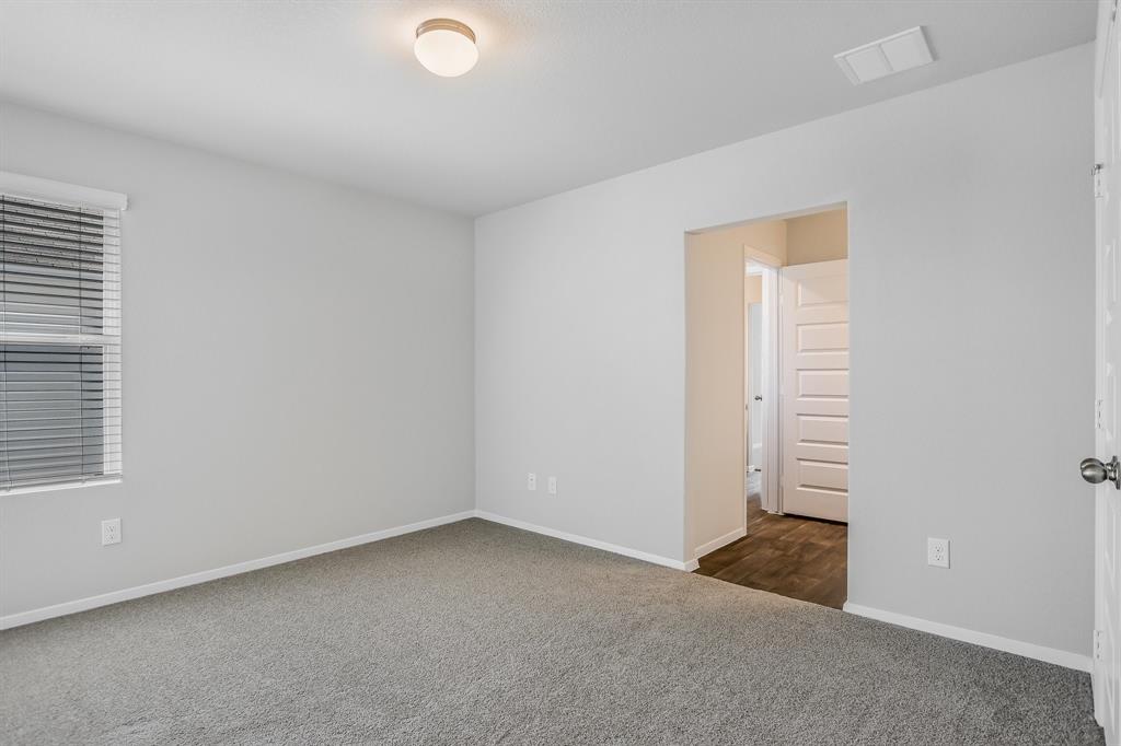 2808 Totley Road Manor, TX 78653 - Photo 11 of 21 Carpeted room with a window featuring horizontal blinds, a flush-mount ceiling light fixture, and an open doorway revealing wood-finish flooring and a paneled door