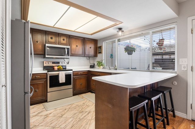 41 Benchmark Village Tooele, UT 84074 - Photo 8 of 26 Kitchen featuring stainless steel appliances, a peninsula, light countertops, a breakfast bar, and dark wood finish cabinetry