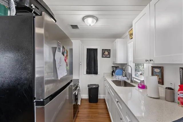a kitchen with stainless steel appliances a sink dishwasher a refrigerator and white cabinets with wooden floor