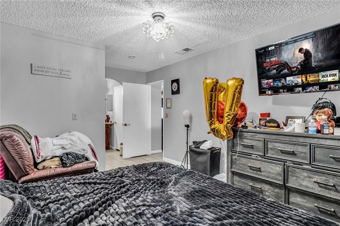 2200 South Fort Apache Road, Unit 1007 Las Vegas, NV 89117 - Photo 14 of 30 Bedroom featuring arched walkways, light tile patterned floors, visible vents, a textured ceiling, and baseboards