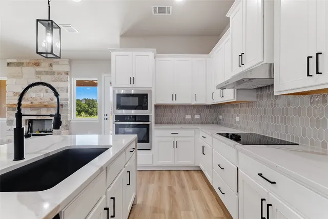 a kitchen with granite countertop a sink stainless steel appliances and white cabinets