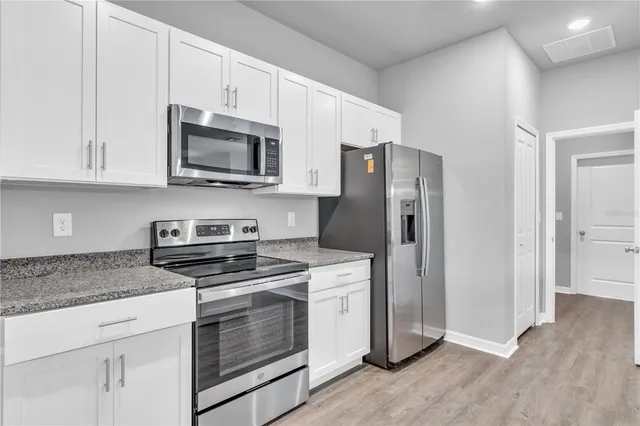 a kitchen with stainless steel appliances white cabinets and a stove a refrigerator with wooden floor