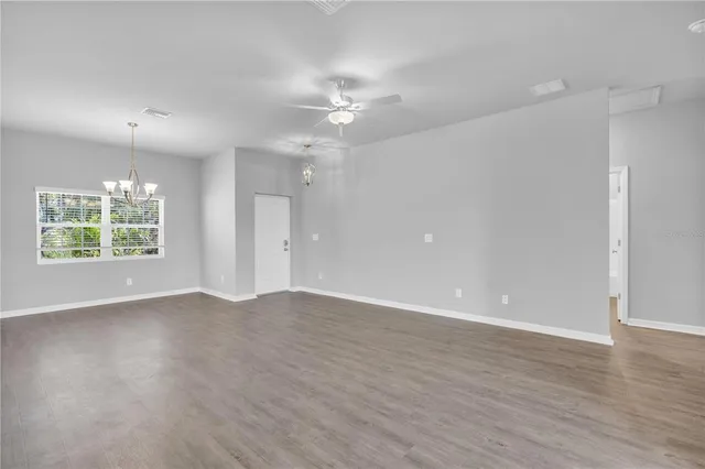 an empty room with wooden floor chandelier fan and windows