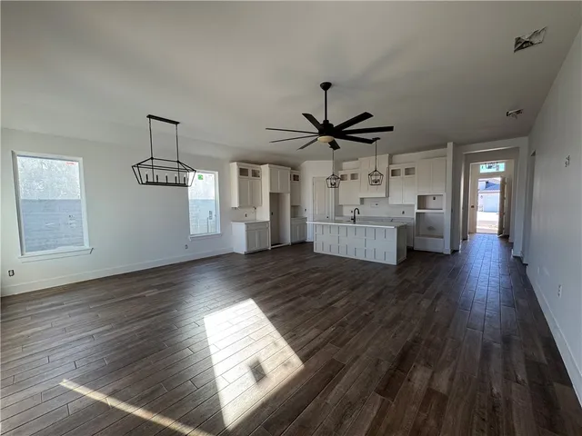 a view of an empty room and kitchen with wooden floor