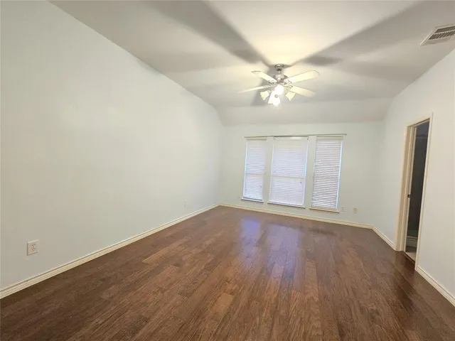 an empty room with wooden floor fan and windows
