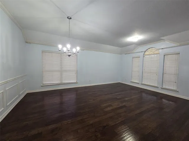 an empty room with wooden floor chandelier fan and windows