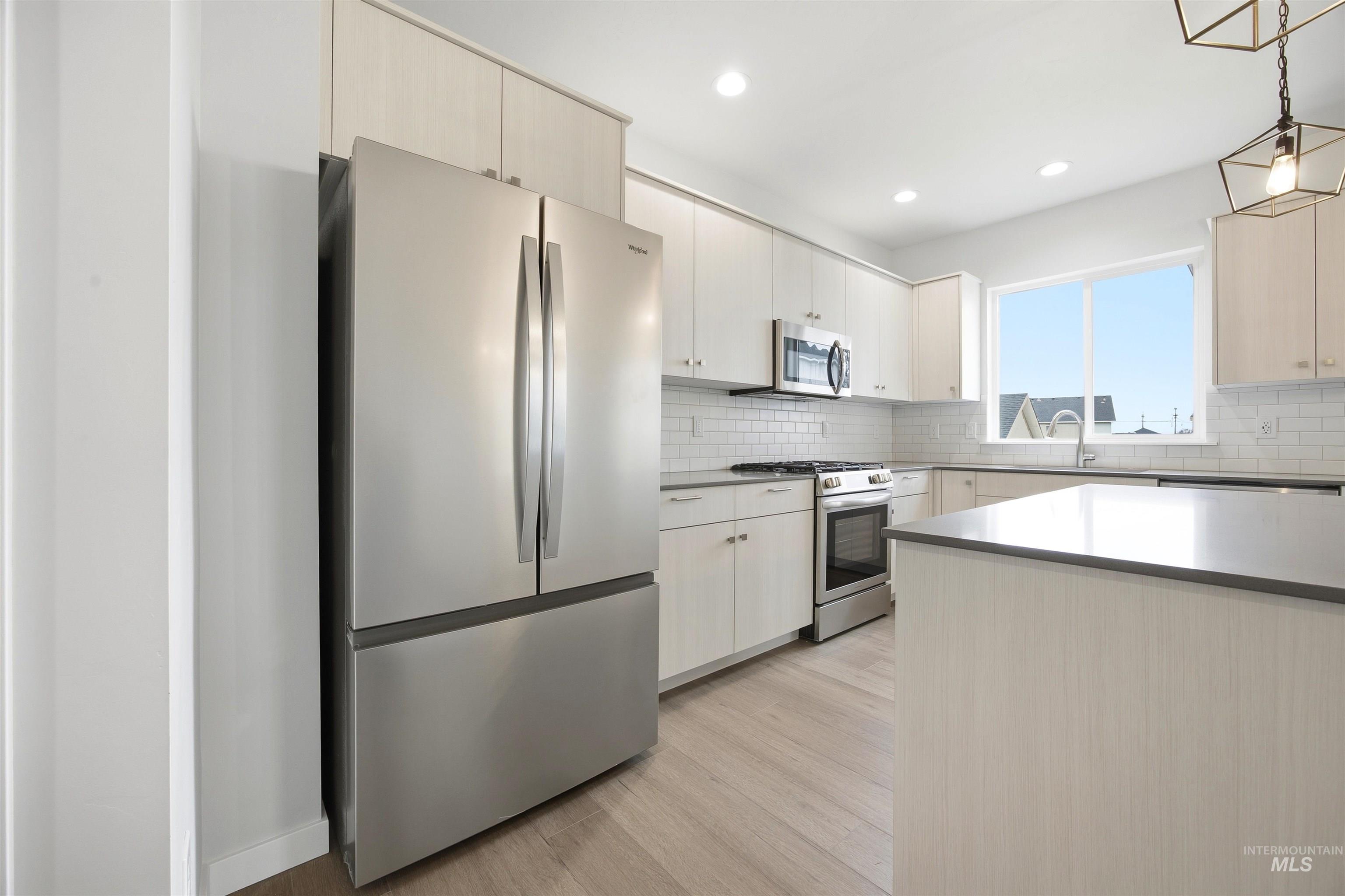 6447 South Sunfish Way Boise, ID 83709 - Photo 6 of 29 Modern kitchen featuring stainless steel appliances, light wood-finish cabinetry, a subway tile backsplash, a center island with a solid surface countertop, and wood-finish flooring