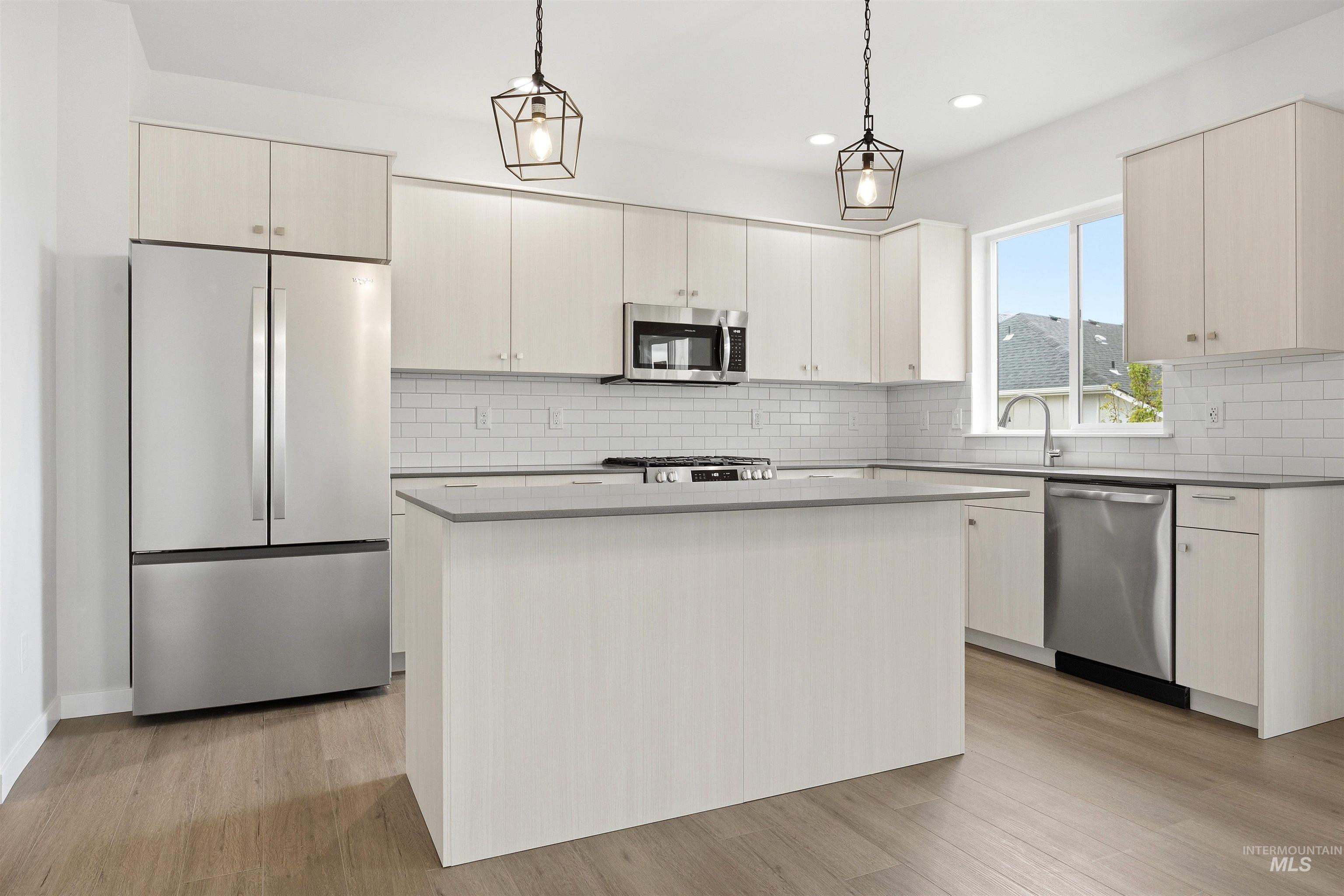 6447 South Sunfish Way Boise, ID 83709 - Photo 7 of 29 Modern kitchen featuring light wood-finish cabinetry, stainless steel appliances, a center island, subway tile backsplash, and dark countertops