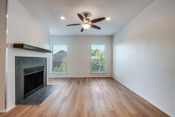 an empty room with wooden floor a ceiling fan a fireplace and windows