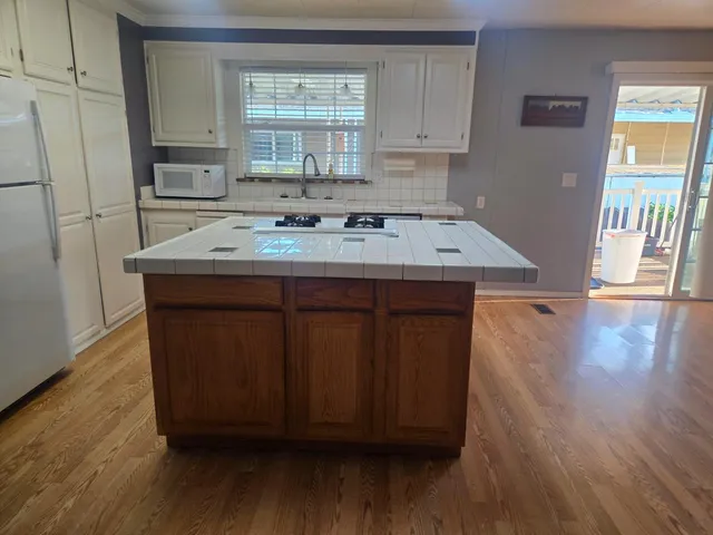 a kitchen with kitchen island wooden floors wooden cabinets a sink and a refrigerator