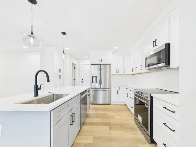 a kitchen with stainless steel appliances granite countertop a stove a sink a refrigerator and white cabinets with wooden floor