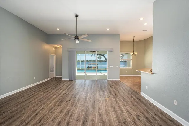 a view of an empty room and kitchen with wooden floor