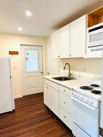 a kitchen with sink a stove and white cabinets with wooden floor