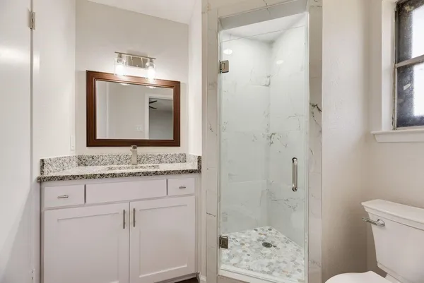 a bathroom with a granite countertop sink a toilet a mirror and shower