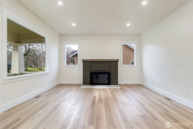 an empty room with wooden floor fireplace and windows