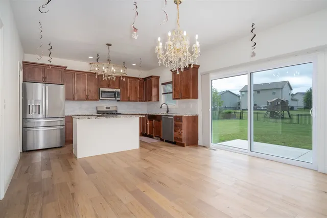 a open kitchen with stainless steel appliances granite countertop a refrigerator oven a sink dishwasher a dining table and chairs with wooden floor