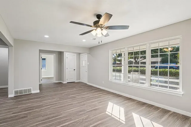 a view of an empty room with wooden floor and a ceiling fan