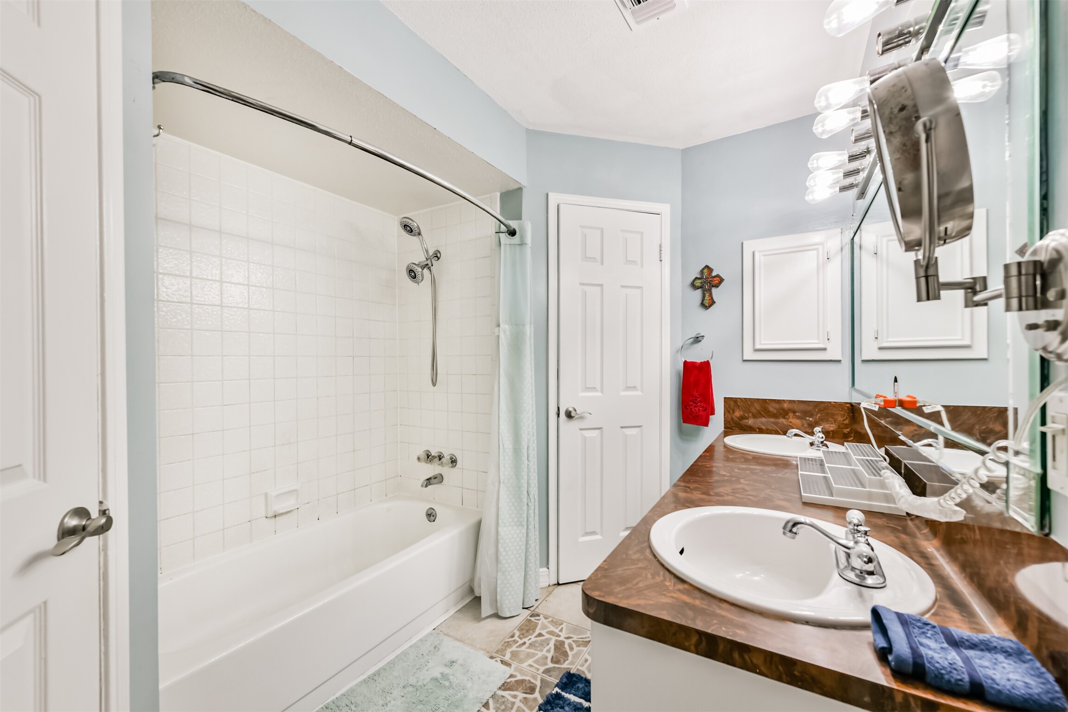 15105 Silverman Street Houston, TX 77598 - Photo 15 of 26 The primary bathroom features a spacious double-sink vanity with a large mirror, complemented by a ceramic tile-enclosed tub and shower for a polished and functional design.