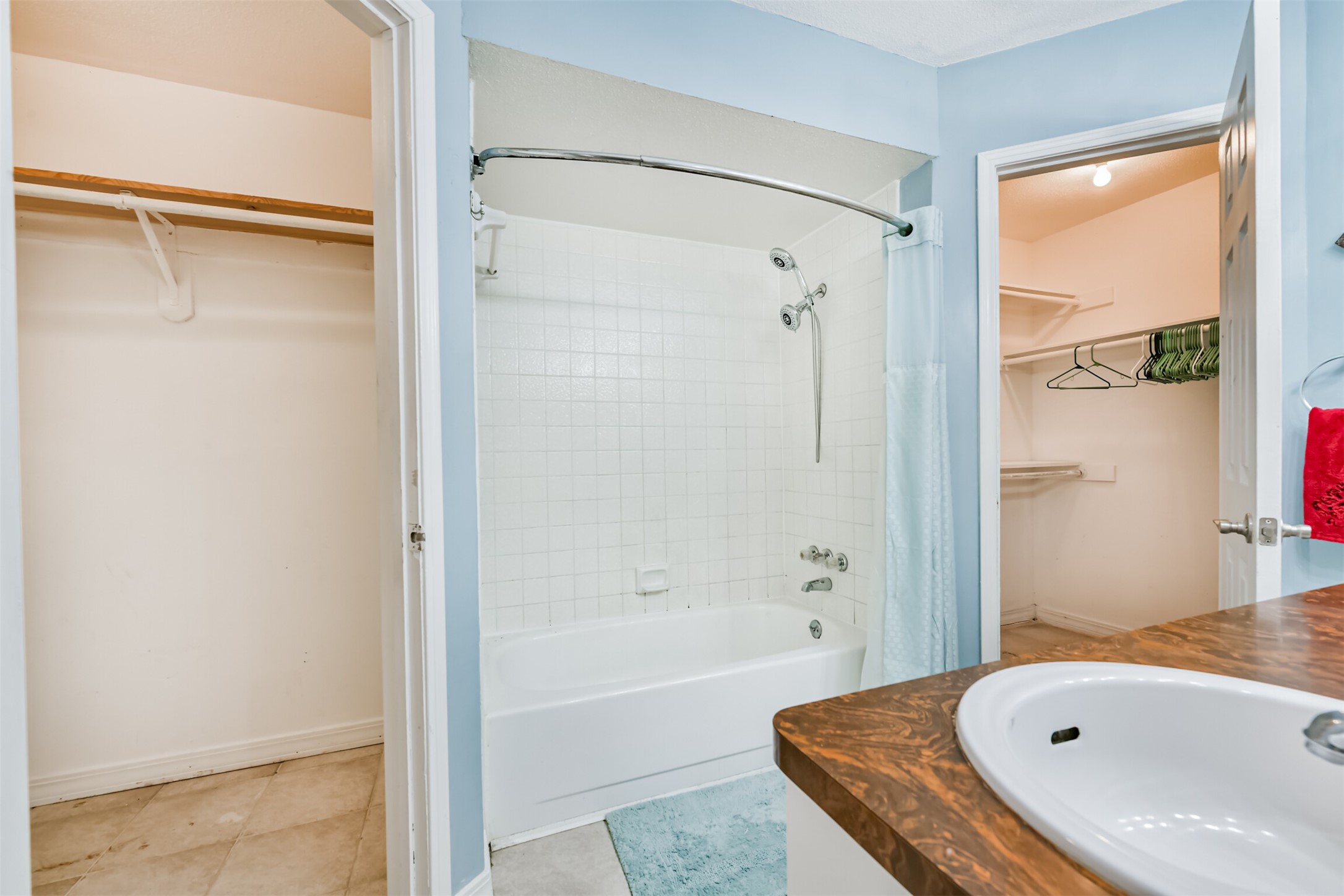 15105 Silverman Street Houston, TX 77598 - Photo 18 of 26 The primary bathroom features a ceramic-tiled tub and shower enclosure, alongside a walk-in closet equipped with shelving and wooden dowels for clothing storage.