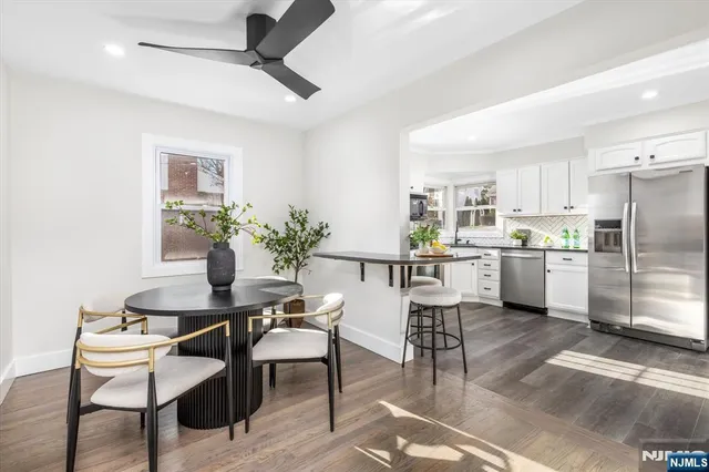 a kitchen with stainless steel appliances kitchen island granite countertop a dining table chairs and a refrigerator