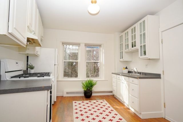 a kitchen with stainless steel appliances granite countertop a stove a sink dishwasher and white cabinets with wooden floor