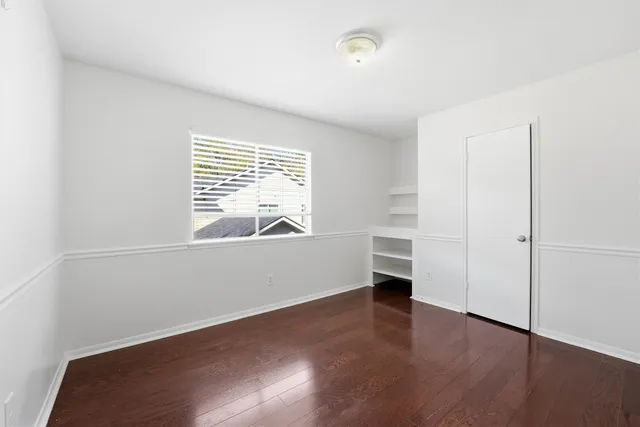 an empty room with wooden floor cabinet and windows