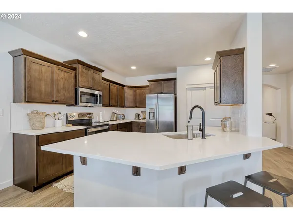 a kitchen with stainless steel appliances a sink a stove a refrigerator cabinets and chairs