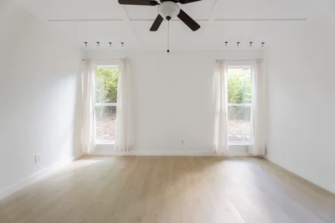 an empty room with wooden floor fan and windows