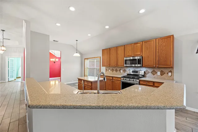 a kitchen with stainless steel appliances granite countertop a sink a stove and a wooden cabinets