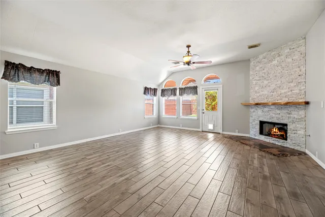an empty room with windows fireplace and wooden floor