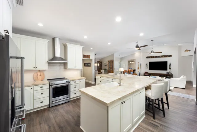a kitchen with stainless steel appliances kitchen island granite countertop a stove a sink a refrigerator and white cabinets with wooden floor