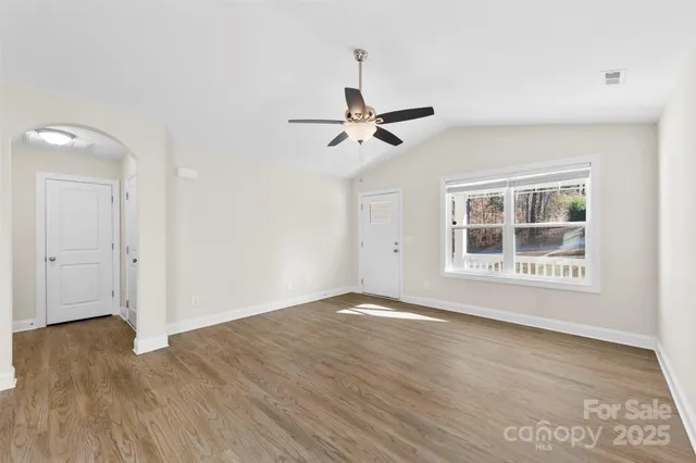 a view of an empty room with wooden floor and a ceiling fan