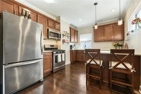 a kitchen with stainless steel appliances granite countertop a refrigerator a stove a sink a dining table and chairs with wooden floor