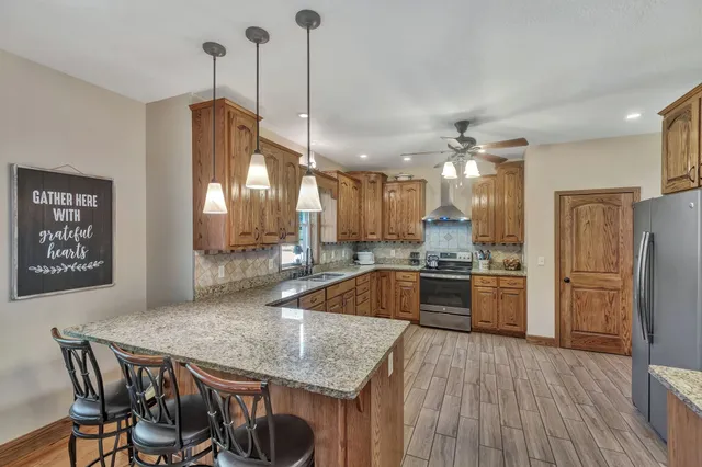 a kitchen with stainless steel appliances granite countertop a kitchen island a stove a refrigerator a sink a dining table and chairs with wooden floor