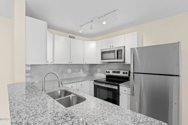 a kitchen with granite countertop a refrigerator sink and white cabinets