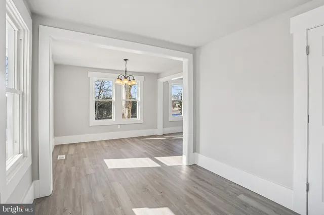 an empty room with wooden floor chandelier and windows