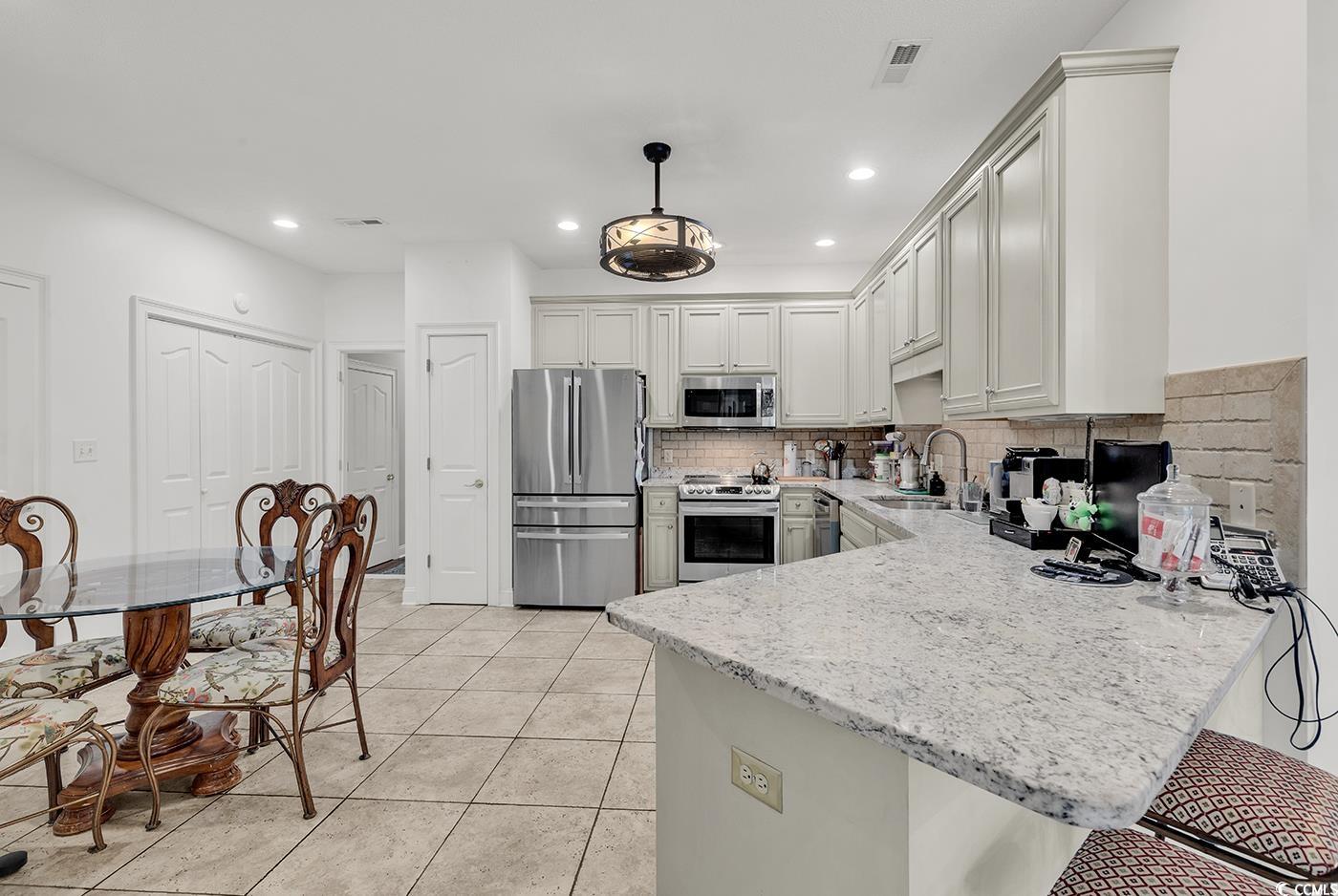 1459 St Thomas Circle, Unit F2 Myrtle Beach, SC 29577 - Photo 3 of 31 Kitchen featuring stainless steel appliances, granite countertops, tile floors, backsplash, and a breakfast bar