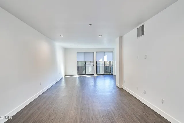 a view of empty room with wooden floor and kitchen