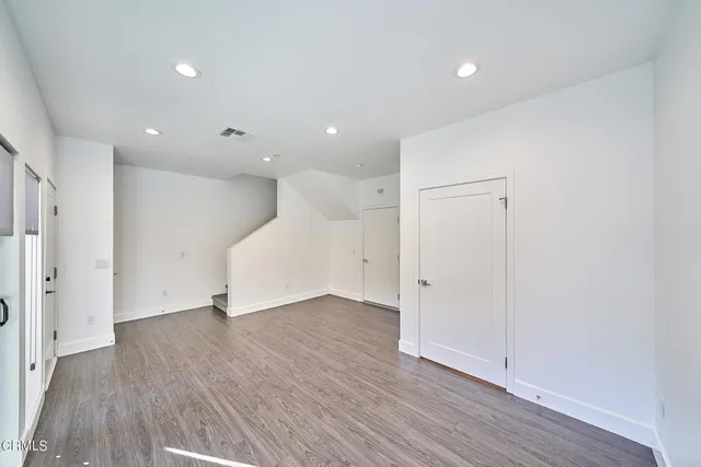 a view of an empty room with wooden floor and a hallway