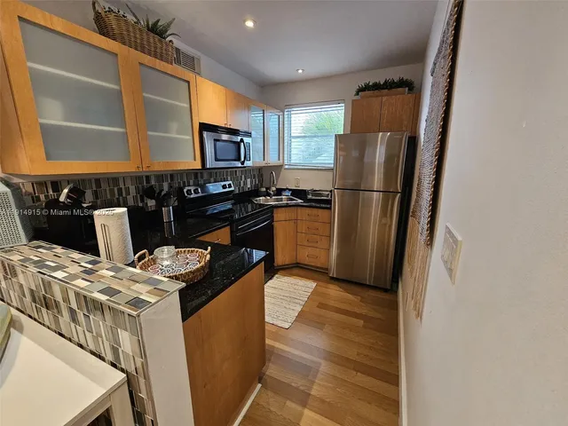 a kitchen with stainless steel appliances granite countertop a refrigerator a stove a sink dishwasher and white cabinets with wooden floor