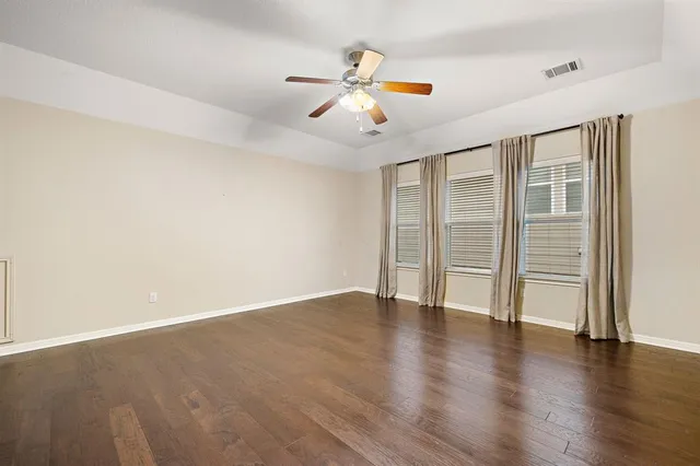 an empty room with wooden floor fan and windows