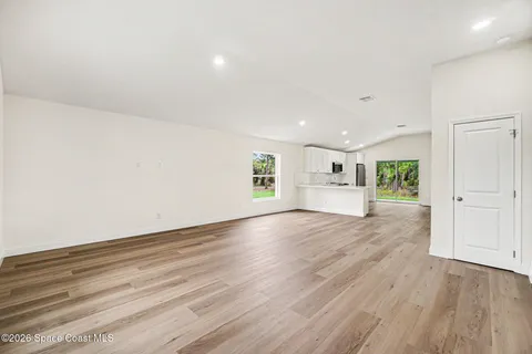 an empty room with wooden floor kitchen view and windows