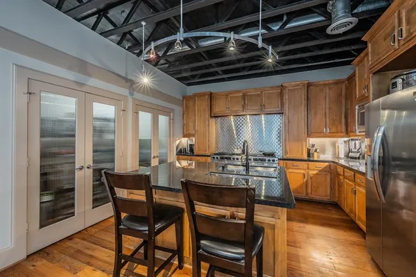 a kitchen with stainless steel appliances kitchen island granite countertop a refrigerator a stove a dining table and chairs with wooden floor