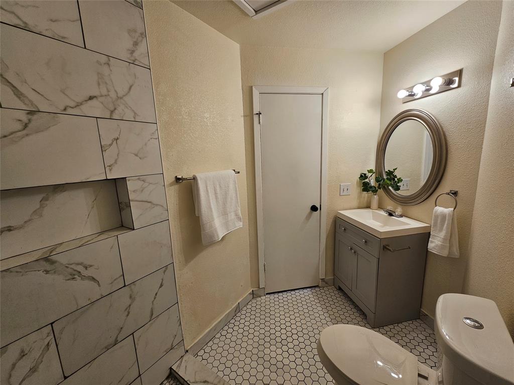 5550 Spring Valley Road, Unit C14 Dallas, TX 75254 - Photo 18 of 21 Modern bathroom featuring a tiled shower with a built-in niche, white hexagonal floor tiles, a gray vanity with an integrated sink, and an oval mirror