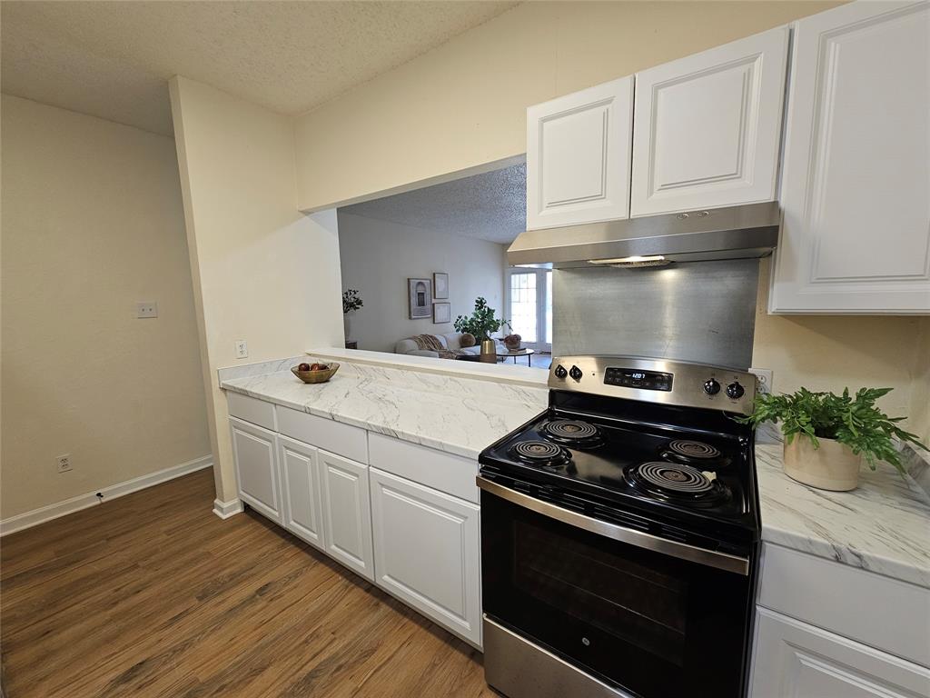 5550 Spring Valley Road, Unit C14 Dallas, TX 75254 - Photo 10 of 21 Kitchen featuring wood-finish flooring, white cabinetry, a stainless steel range with overhead hood, and light-toned countertops