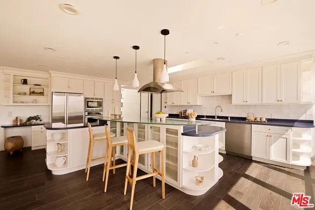 a kitchen with stainless steel appliances kitchen island granite countertop a stove a sink and white cabinets with wooden floor