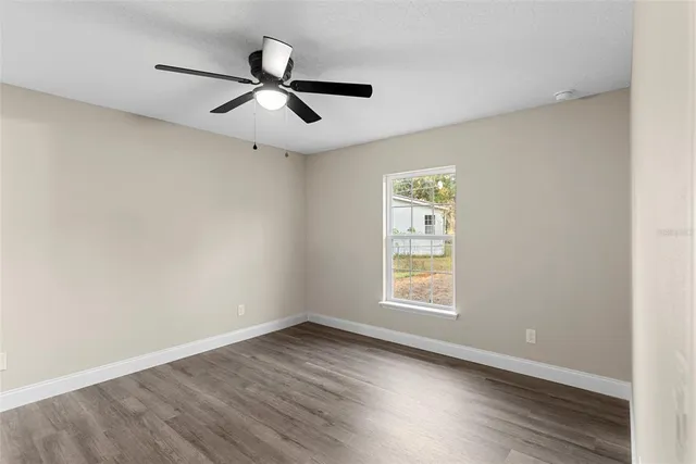 an empty room with wooden floor ceiling fan and windows